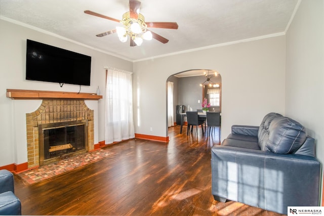 living area featuring crown molding, baseboards, wood finished floors, arched walkways, and a ceiling fan