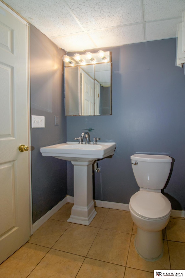 bathroom with a drop ceiling, baseboards, toilet, and tile patterned flooring