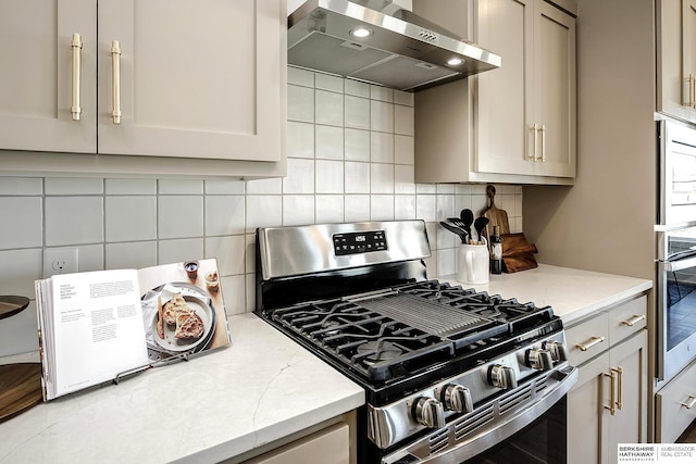 kitchen featuring light stone counters, backsplash, appliances with stainless steel finishes, and exhaust hood