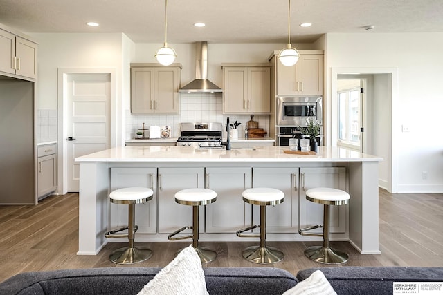 kitchen with tasteful backsplash, wall chimney range hood, light countertops, wood finished floors, and stainless steel appliances