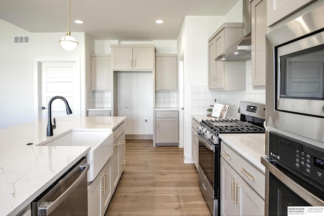 kitchen with light stone countertops, visible vents, light wood-style flooring, stainless steel appliances, and wall chimney range hood