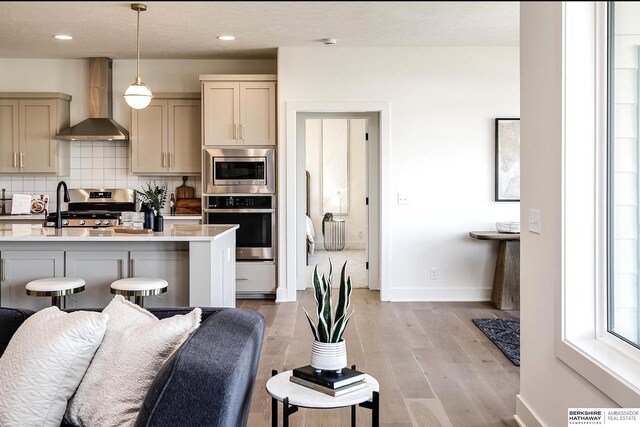 kitchen featuring light wood-type flooring, light countertops, appliances with stainless steel finishes, wall chimney range hood, and tasteful backsplash
