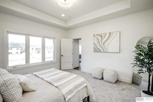 carpeted bedroom featuring a raised ceiling and baseboards