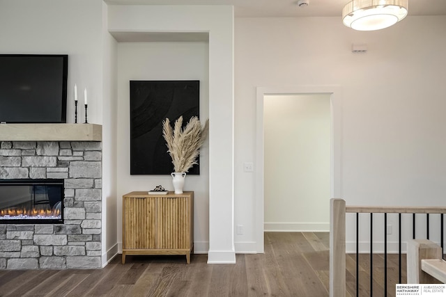 living area featuring a stone fireplace, baseboards, and wood finished floors