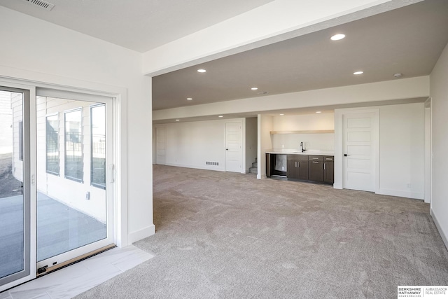 unfurnished living room with a sink, recessed lighting, wet bar, baseboards, and light colored carpet