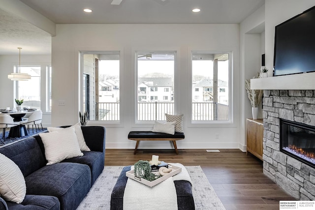 living area featuring a stone fireplace, plenty of natural light, and dark wood-style flooring