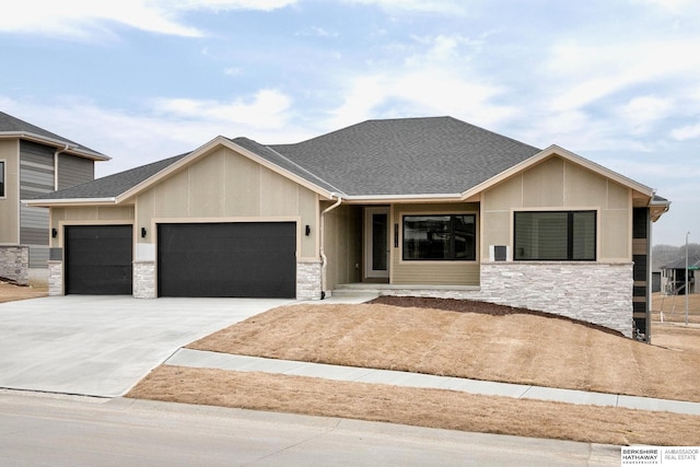 view of front facade featuring a garage, stone siding, roof with shingles, and concrete driveway