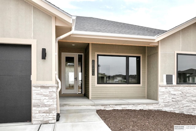 view of exterior entry featuring stucco siding, stone siding, a garage, and a shingled roof