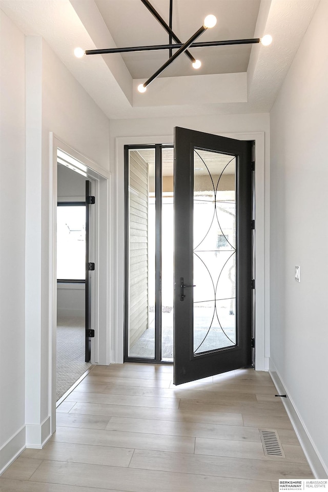 entryway with visible vents, a tray ceiling, light wood-type flooring, and baseboards