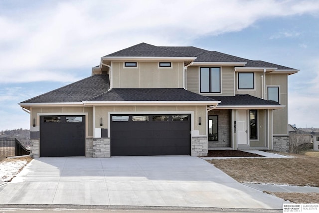 prairie-style home featuring fence, an attached garage, a shingled roof, concrete driveway, and stone siding