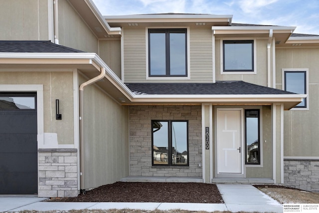 doorway to property featuring stone siding and a shingled roof