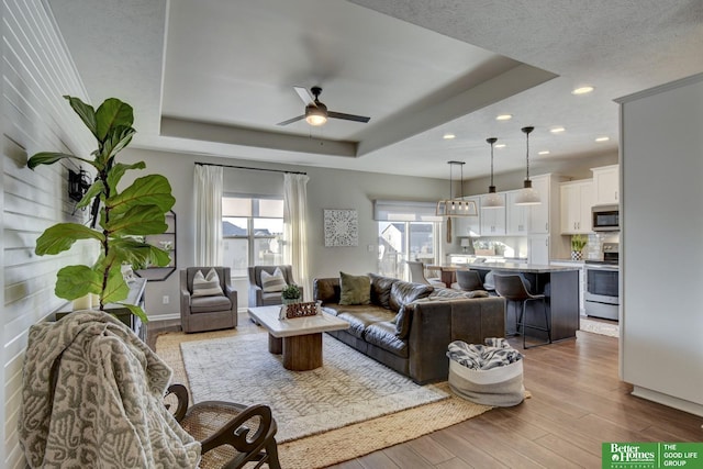 living area with a ceiling fan, a tray ceiling, a textured ceiling, wood finished floors, and recessed lighting