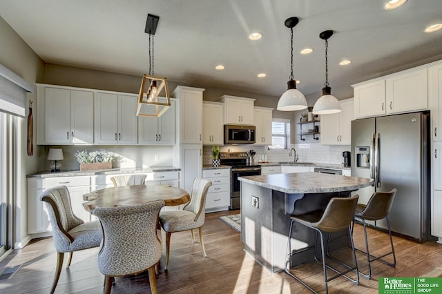 kitchen featuring a sink, a kitchen island, wood finished floors, white cabinetry, and appliances with stainless steel finishes