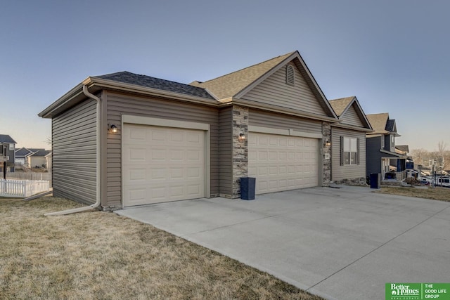 exterior space featuring fence, roof with shingles, a garage, stone siding, and driveway