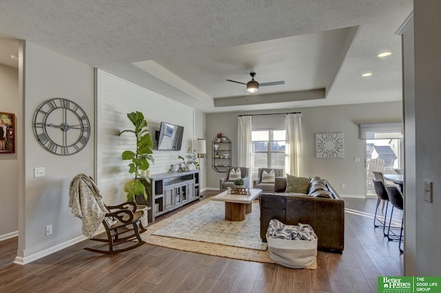 living room with baseboards, a raised ceiling, dark wood-type flooring, and ceiling fan