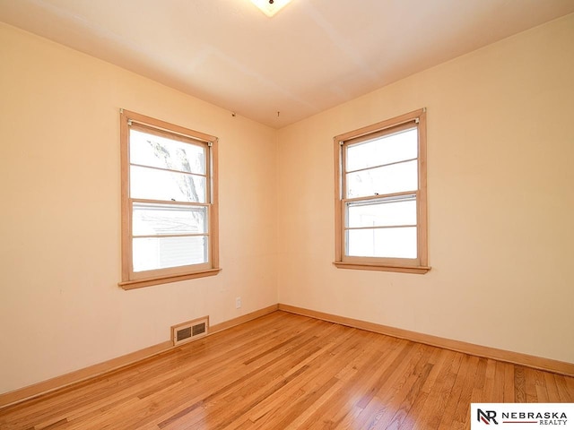 empty room featuring a wealth of natural light, visible vents, baseboards, and light wood-style flooring