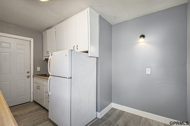 kitchen featuring wood finished floors, baseboards, freestanding refrigerator, light countertops, and white cabinetry