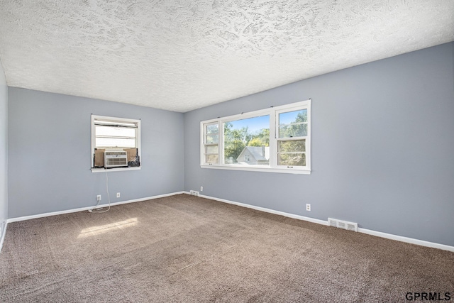 carpeted empty room with visible vents, cooling unit, a textured ceiling, and baseboards