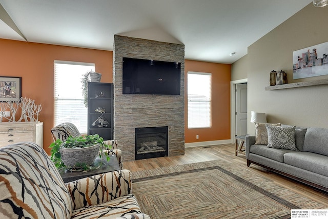 living area featuring a stone fireplace, vaulted ceiling, wood finished floors, and baseboards