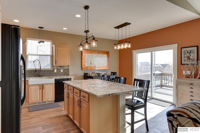 kitchen featuring light brown cabinetry, a breakfast bar area, light countertops, black appliances, and a sink