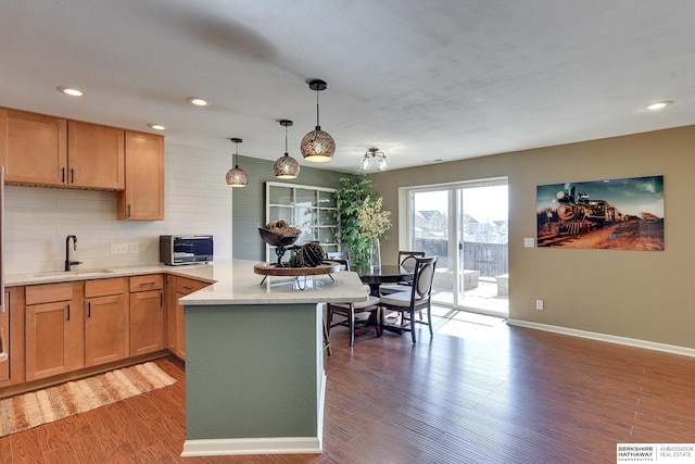 kitchen featuring wood finished floors, a peninsula, a sink, light countertops, and backsplash