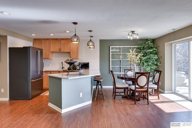 kitchen with a peninsula, high end fridge, light countertops, light wood-style floors, and pendant lighting