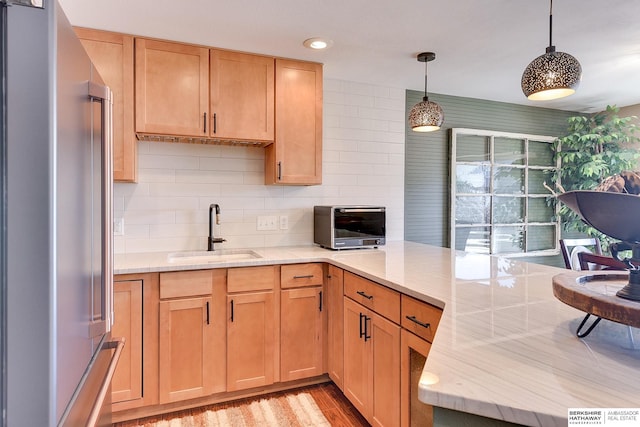 kitchen with tasteful backsplash, light stone countertops, a peninsula, high quality fridge, and a sink