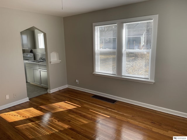 unfurnished dining area featuring arched walkways, visible vents, dark wood-type flooring, and baseboards