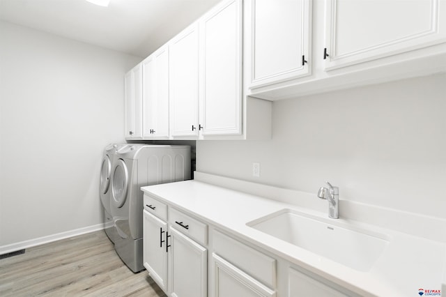 laundry area featuring washing machine and clothes dryer, visible vents, light wood-style floors, cabinet space, and a sink