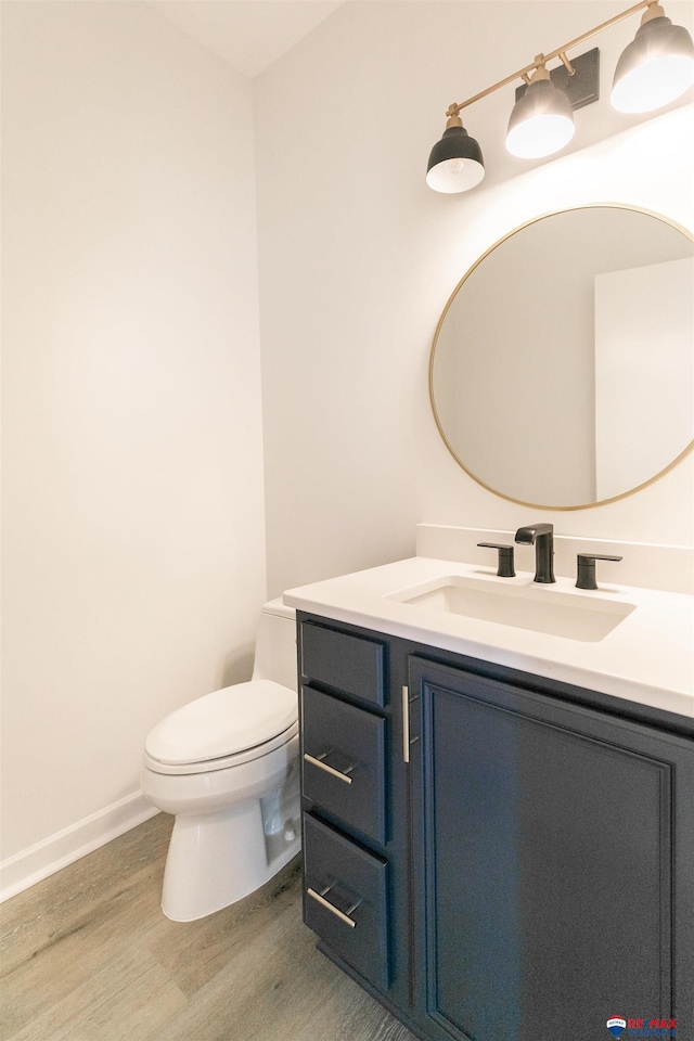 half bathroom featuring baseboards, toilet, wood finished floors, and vanity