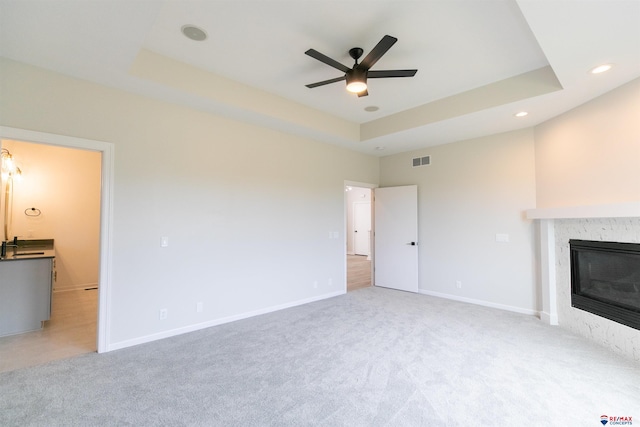 unfurnished living room featuring a ceiling fan, baseboards, carpet floors, a tray ceiling, and a high end fireplace