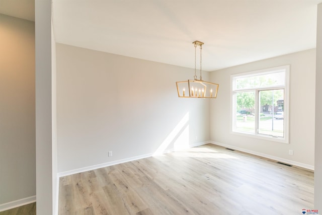 empty room featuring an inviting chandelier, wood finished floors, visible vents, and baseboards