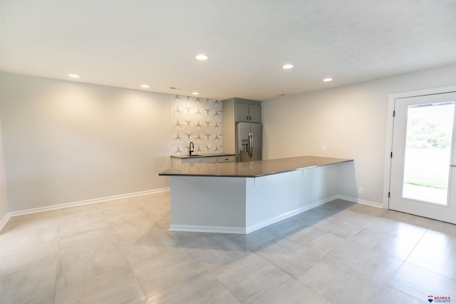 kitchen with baseboards, a peninsula, recessed lighting, a sink, and stainless steel fridge