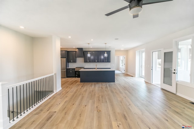 kitchen with a kitchen island with sink, range hood, freestanding refrigerator, light wood-style floors, and decorative backsplash