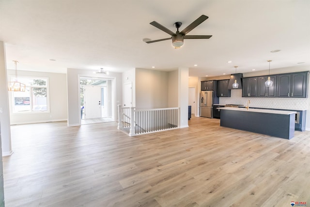 kitchen with open floor plan, stainless steel fridge, wall chimney range hood, and a kitchen island with sink