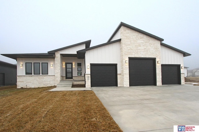 view of front of property with board and batten siding, concrete driveway, a front yard, a garage, and stone siding