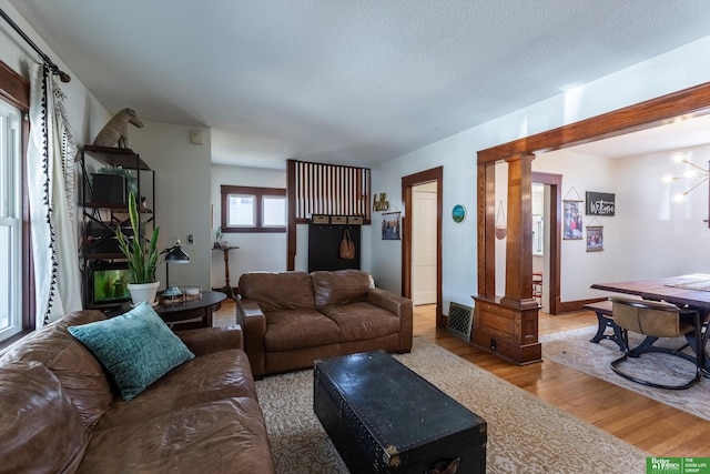 living area with decorative columns, a textured ceiling, wood finished floors, and a chandelier