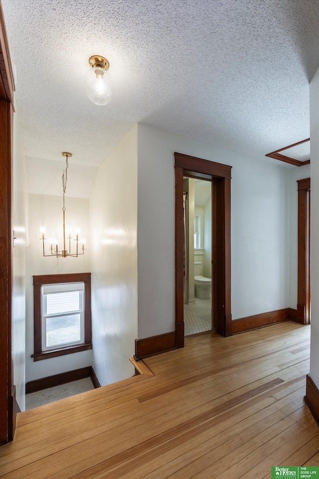 hall featuring a textured ceiling, baseboards, wood-type flooring, and a chandelier