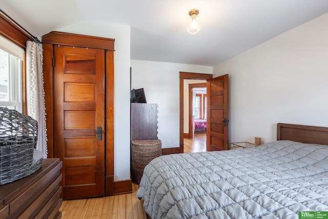 bedroom featuring light wood-type flooring, baseboards, and vaulted ceiling