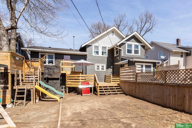 rear view of property with fence and a playground