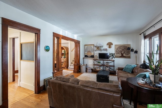 living area featuring light wood-style flooring, baseboards, arched walkways, and a textured ceiling