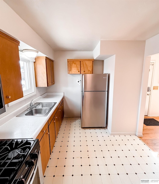 kitchen with brown cabinetry, light floors, freestanding refrigerator, a sink, and light countertops