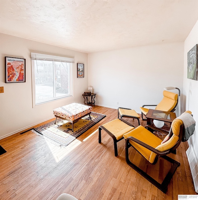 living area featuring light wood-style flooring, baseboards, visible vents, and a textured ceiling