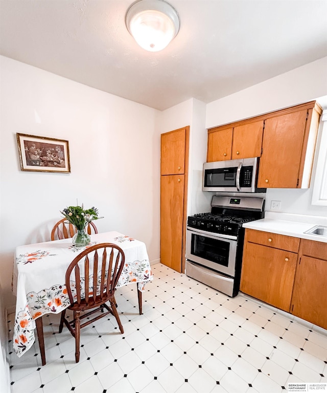 kitchen featuring stainless steel appliances, light floors, brown cabinetry, and light countertops