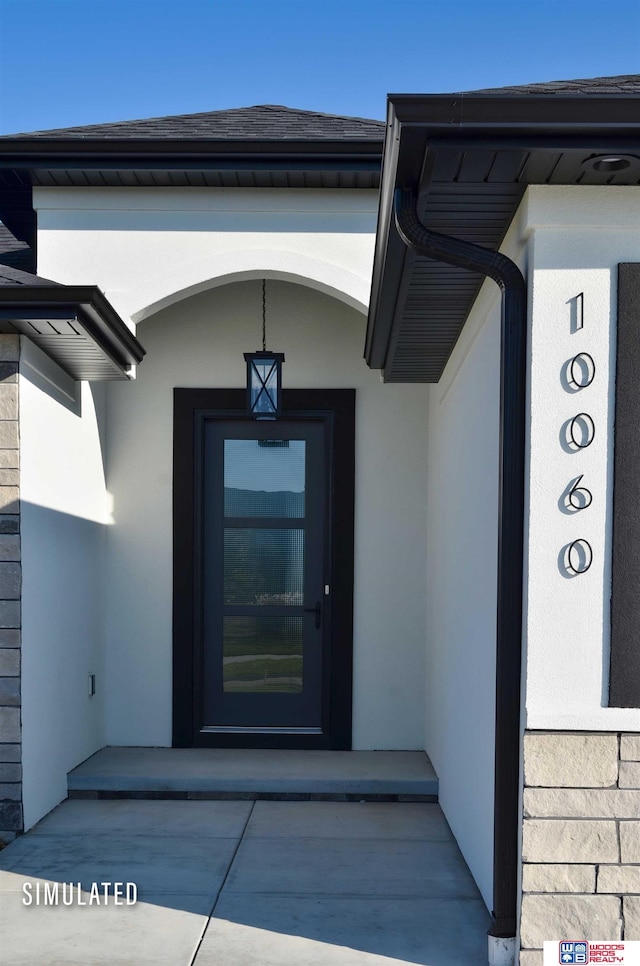 doorway to property featuring stucco siding and roof with shingles