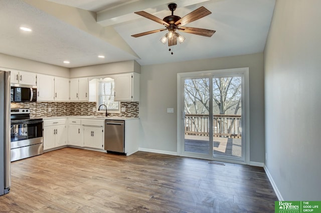 kitchen with backsplash, baseboards, lofted ceiling with beams, appliances with stainless steel finishes, and light wood-style floors