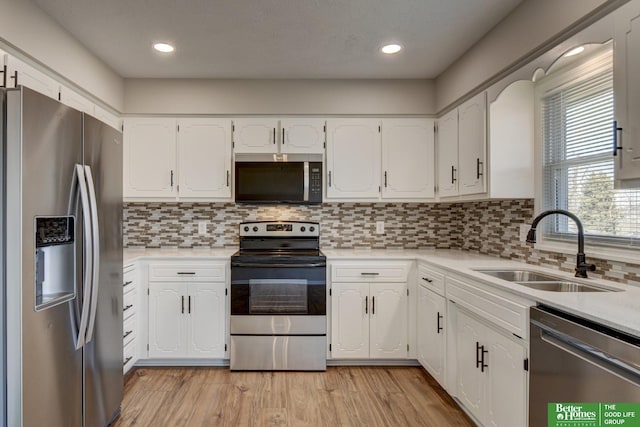 kitchen with white cabinets, stainless steel appliances, light wood-type flooring, and a sink