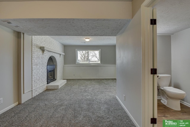 unfurnished living room with a textured ceiling, carpet, visible vents, a fireplace, and wainscoting