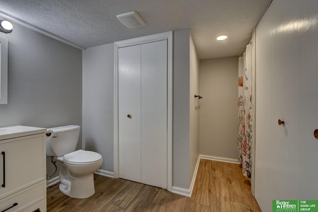 bathroom featuring wood finished floors, baseboards, visible vents, a textured ceiling, and toilet