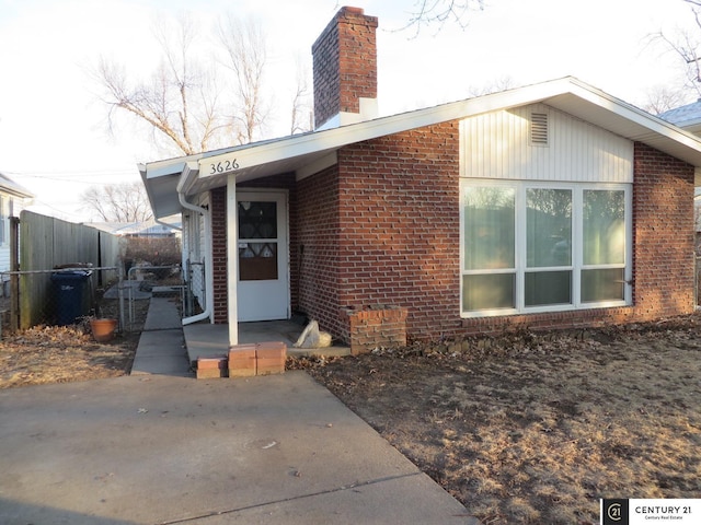 view of exterior entry with brick siding, a chimney, and fence